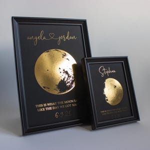 May include: Two framed prints with black frames and black backgrounds. The larger print has the names "Angela & Jordan" in gold script above a gold foil moon. The smaller print has the name "Stephan" above a gold foil moon.