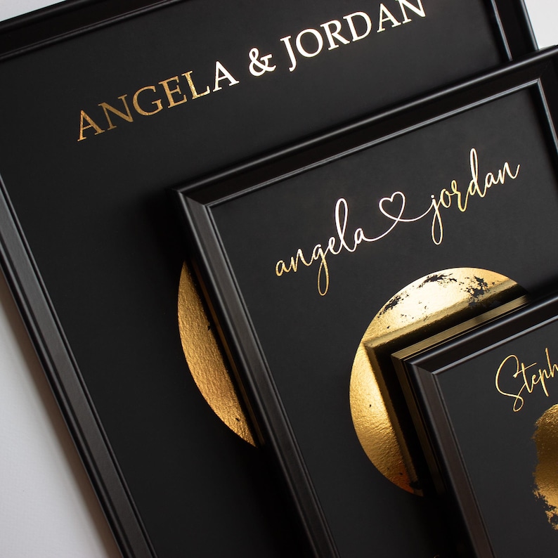 May include: Three framed black art pieces with gold lettering and accents. The top frame reads "ANGELA & JORDAN" in gold. The middle frame has "angela & jordan" in gold script. The bottom frame has a gold heart shape.