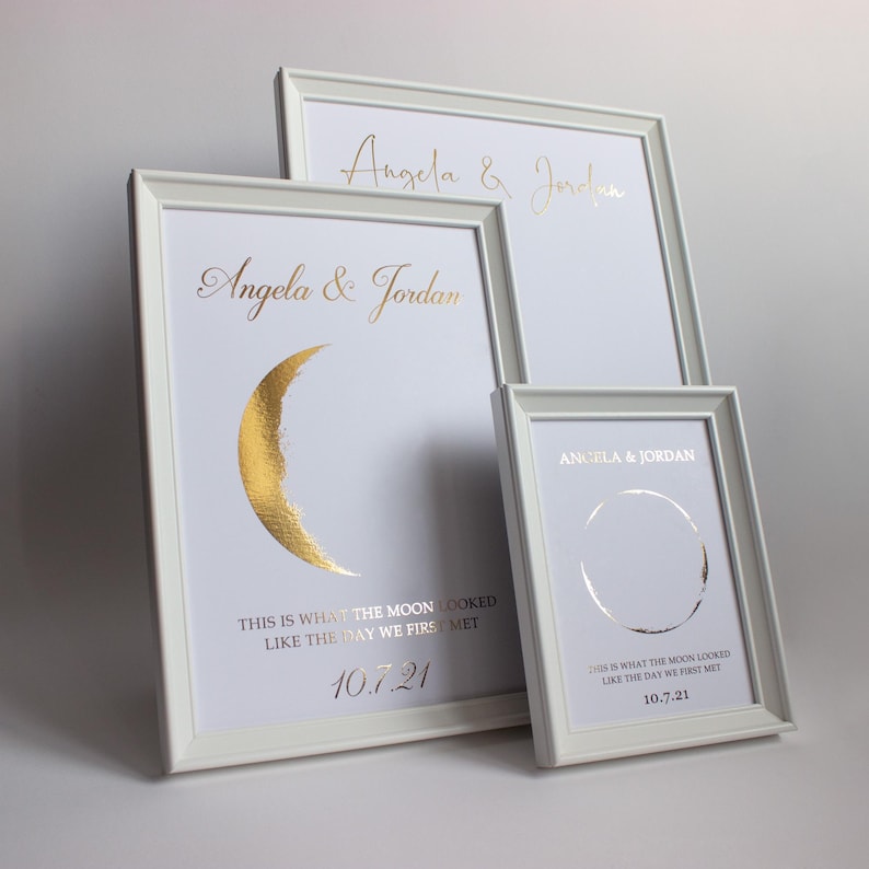 May include: Three white framed prints with gold foil text and designs. The prints feature the names "Angela & Jordan", a crescent moon, and the date "10.7.21". The text reads "THIS IS WHAT THE MOON LOOKED LIKE THE DAY WE FIRST MET".
