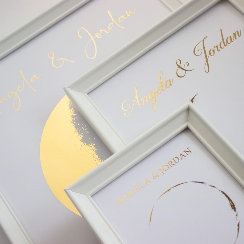 May include: White framed prints with gold foil text that reads "Angela & Jordan". The prints feature a gold foil half-circle design and a gold foil circle. The frames are white and the background is white.