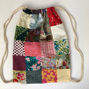 May include: A patchwork drawstring bag with a variety of colorful patterns, including floral, geometric, and animal prints. The bag is made of fabric and has a white drawstring.