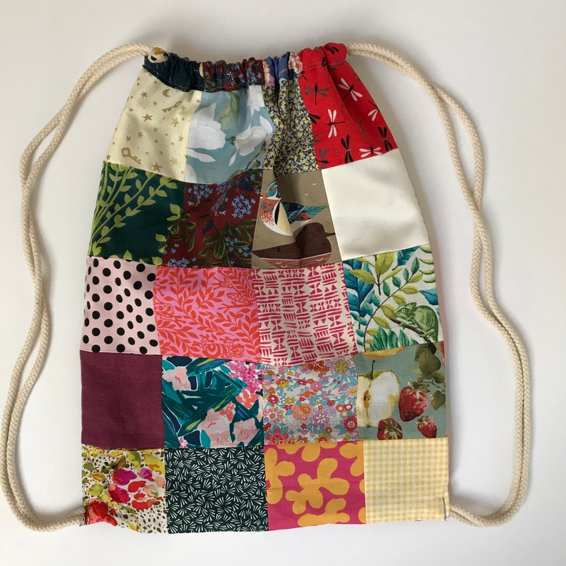 May include: A patchwork drawstring bag with a variety of colorful patterns, including floral, geometric, and animal prints. The bag is made of fabric and has a white drawstring.