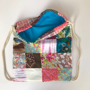 May include: A patchwork drawstring bag with a blue lining. The bag is made of various colorful fabrics with floral and geometric patterns.