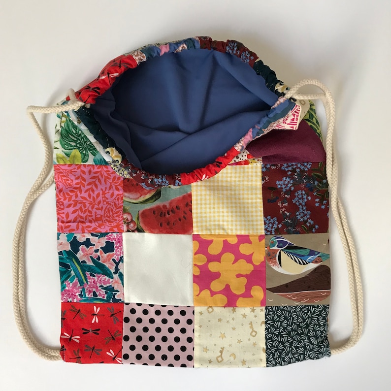May include: A patchwork drawstring bag with a blue lining. The bag is made of various fabrics with different patterns, including floral, geometric, and animal prints. The bag has a white drawstring.