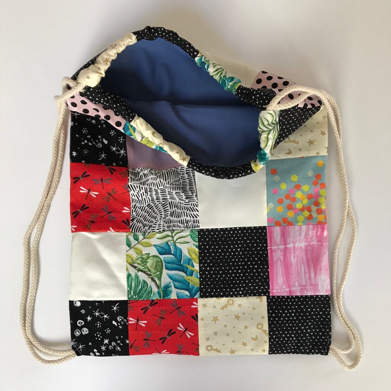 Pode incluir: Uma bolsa de cord&atilde;o de retalhos com uma variedade de padr&otilde;es coloridos, incluindo estrelas, lib&eacute;lulas e desenhos geom&eacute;tricos. A bolsa &eacute; feita de tecido de algod&atilde;o e tem um forro azul.