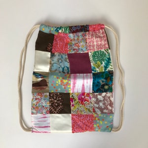 Peut inclure: Un sac à cordon en patchwork avec une variété de motifs floraux et géométriques dans des tons de rose, bleu, vert, marron et blanc.