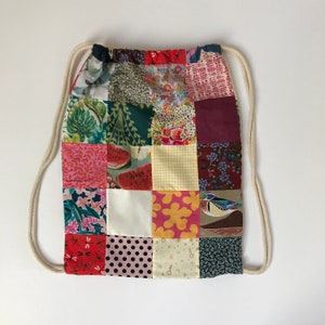 Peut inclure: Un sac à cordon en patchwork avec une variété de motifs colorés, y compris des imprimés floraux, géométriques et animaliers. Le sac a un cordon blanc et est fait de tissu.