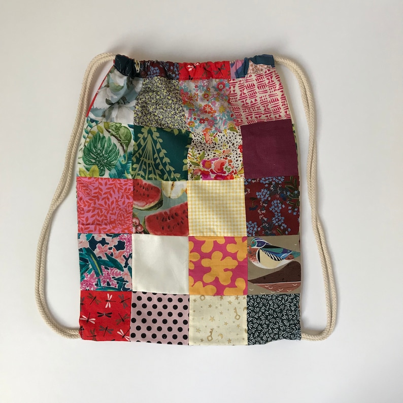 May include: A patchwork drawstring bag with a variety of colorful patterns, including floral, geometric, and animal prints. The bag has a white drawstring and is made of fabric.