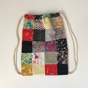 Peut inclure: Un sac à cordon en tissu patchwork avec une variété de motifs colorés, y compris des imprimés floraux, géométriques et animaliers. Le sac a un cordon blanc et est en coton.