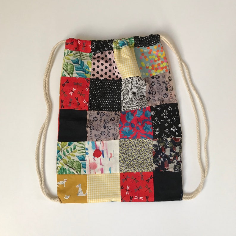 Puede incluir: Una bolsa de cord&oacute;n hecha de tela de patchwork con una variedad de patrones coloridos, incluyendo estampados florales, geom&eacute;tricos y de animales. La bolsa tiene un cord&oacute;n blanco y est&aacute; hecha de algod&oacute;n.