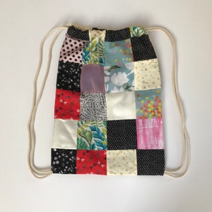 May include: A patchwork drawstring bag with a variety of colorful patterns, including floral, geometric, and abstract designs. The bag is made of fabric and has a white drawstring.