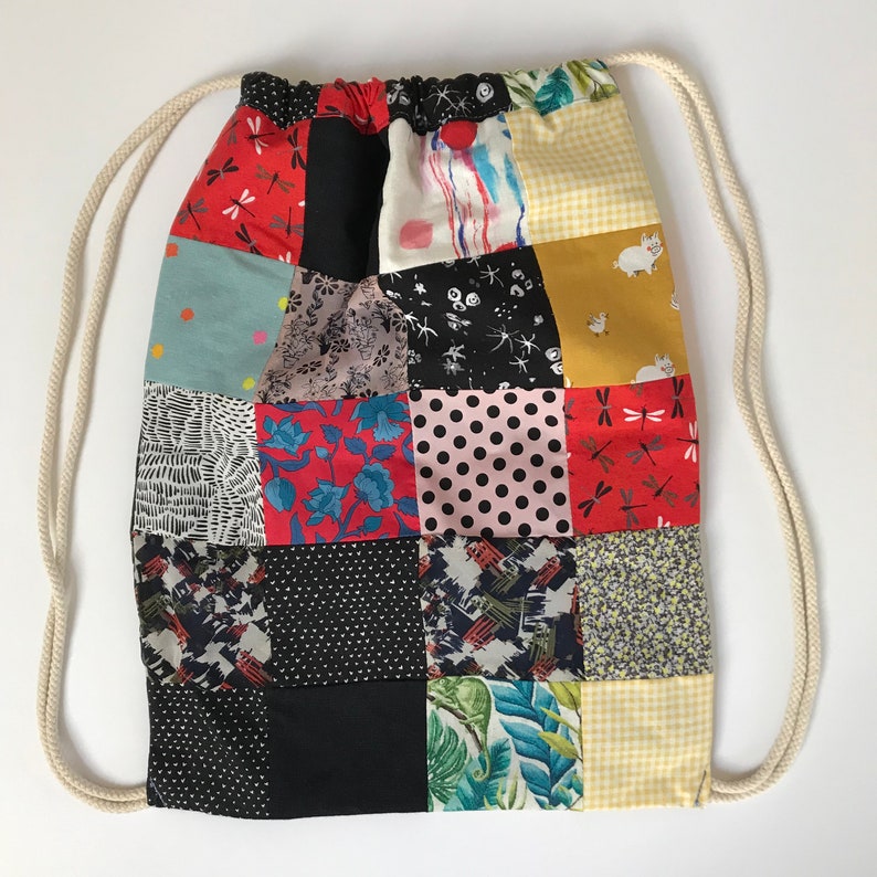 Puede incluir: Una bolsa de cord&oacute;n de retazos con una variedad de cuadrados de tela coloridos. La bolsa est&aacute; hecha de diferentes telas, incluyendo estampados florales, geom&eacute;tricos y de animales. La bolsa tiene un cord&oacute;n blanco y es perfecta para llevar objetos peque&ntilde;os.