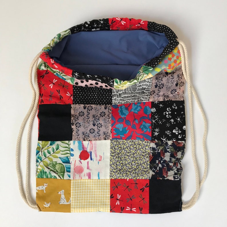 Puede incluir: Una bolsa de cord&oacute;n de retazos con una variedad de cuadrados de tela coloridos. La bolsa est&aacute; hecha de algod&oacute;n y tiene un forro azul. Los cuadrados de tela presentan diferentes patrones, incluyendo dise&ntilde;os florales, geom&eacute;tricos y abstractos.