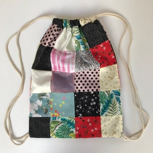 Pode incluir: Uma bolsa de cord&atilde;o de tecido com um design de patchwork com uma variedade de padr&otilde;es coloridos, incluindo flores, bolinhas e desenhos geom&eacute;tricos. A bolsa &eacute; feita de tecido e tem um cord&atilde;o branco.