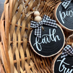 May include: Three black wood slice ornaments with white lettering and black and white checkered ribbon. The ornaments say "faith", "truth", and "pure".