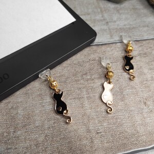 Könnte beinhalten: Drei goldene Katzen-Lesezeichen mit schwarzen, weißen und goldenen Akzenten. Die Charms sind an klaren Plastikclips befestigt.