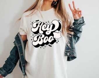 May include: White t-shirt with a black and white graphic design that says "Hey Boo" in a retro font with a ghost illustration.