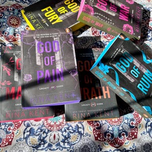 A complete 6-book set of Rina Kent's Legacy of Gods series featuring custom sprayed edges. The book edges are airbrushed in a solid rainbow gradient of red, purple, orange, blue, yellow, and pink to perfectly match the original covers. The books are stacked on a white shelf in a minimalist "BookTok" aesthetic style.