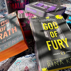 A complete 6-book set of Rina Kent's Legacy of Gods series featuring custom sprayed edges. The book edges are airbrushed in a solid rainbow gradient of red, purple, orange, blue, yellow, and pink to perfectly match the original covers. The books are stacked on a white shelf in a minimalist "BookTok" aesthetic style.