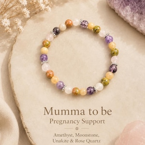 May include: A beaded stretch bracelet featuring alternating round amethyst, moonstone, unakite, and rose quartz beads accented with small silver-toned metal spacers. The text Mumma to be Pregnancy Support Amethyst, Moonstone, Unakite & Rose Quartz is printed below.