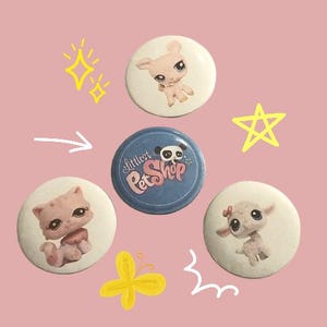 May include: Five colorful round buttons with various images. The buttons feature a pink pig, a panda, a white lamb, a pink cat, and a butterfly. The buttons have the text "Littlest Pet Shop" on one of the buttons.