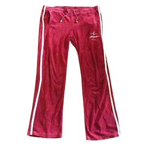May include: Deep red velour sweatpants featuring a white vertical stripe down each outer leg, an elastic waistband with a drawstring, and a white embroidered apple graphic with the text Juicy Couture on the upper left thigh area.