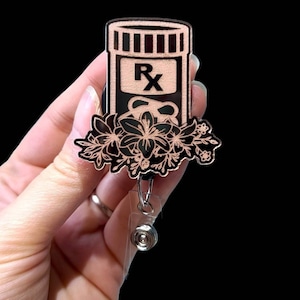 May include: A black and rose gold retractable badge reel with a floral design and a pill bottle with the letters "RX" on it.