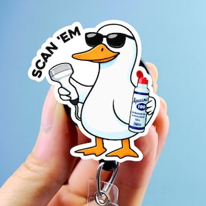 May include: A white duck wearing sunglasses, holding a medical device and a bottle of gel. The duck has orange feet and a beak. The text "SCAN 'EM" is above the duck. The badge reel has a clear plastic strap and a metal clip.