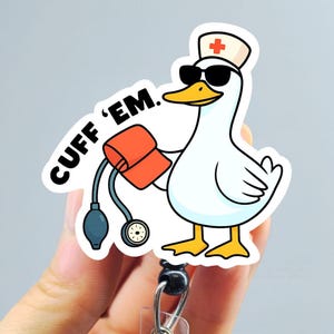 May include: A white badge reel featuring a cartoon goose wearing sunglasses and a nurse's hat, holding a blood pressure cuff. The text "CUFF 'EM" is printed on the badge reel.