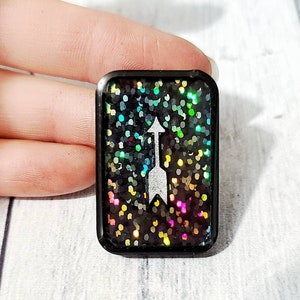 May include: A black square resin keychain with a silver glitter background and a white arrow pointing upwards.