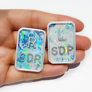 May include: Two white rectangular eye chart stickers with a holographic blue and white background. The left sticker says "L SDP" and the right sticker says "R SDP".