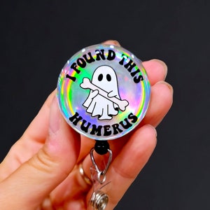 May include: A holographic badge reel with a white ghost holding a bone and the text "I found this humerus".