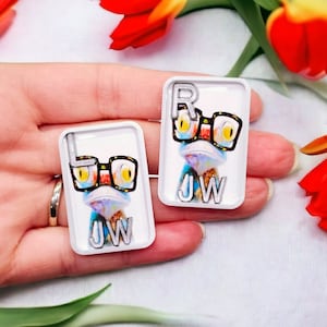 May include: Two white square tiles with a cartoon image of a lizard wearing glasses. The lizard is blue, green, and yellow. The tiles have the letters "JW" and "RW" on them.