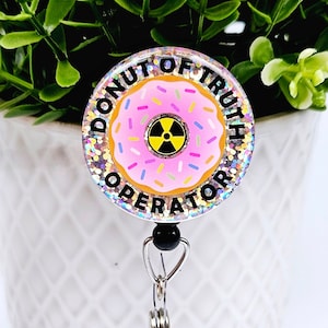 May include: A pink and white donut with sprinkles and a yellow radiation symbol in the centre. The donut is surrounded by a silver glitter background with the text "Donut of Truth Operator" in black.