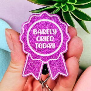 May include: A pink glitter badge holder with a white ribbon and the text "Barely Cried Today".