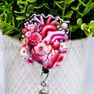 May include: A clear plastic badge holder with a pink anatomical heart surrounded by pink and white flowers. The heart has a red and purple color scheme.