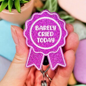 May include: Pink glitter badge holder with a white ribbon and the text "Barely Cried Today".