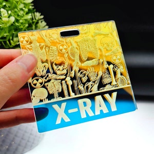 May include: A blue and yellow plastic badge featuring a skeleton design and the text "X-RAY" printed on it.