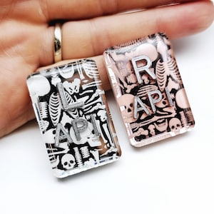 May include: Two small rectangular resin pieces with a skeleton pattern and the letters "L API" and "R API" in silver lettering.