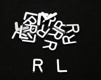 May include: A close-up of a black surface with white plastic letters spelling out the word "RL" with a pile of white plastic letters in the background.