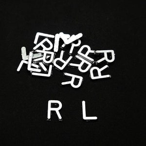 May include: A close-up of a black surface with white plastic letters spelling out the word "RL" with a pile of white plastic letters in the background.