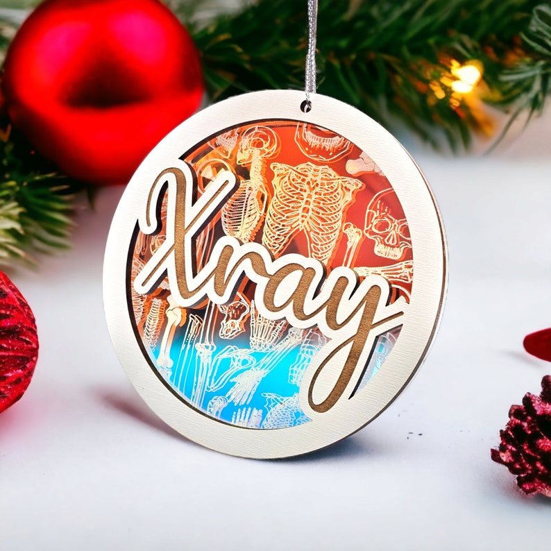 May include: Round Christmas ornament with a silver frame and the word "Xray" in wooden script. The ornament features a layered design with a skeleton illustration and a gradient of orange, blue, and white colors. A silver string is attached for hanging.