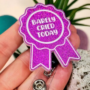 May include: A pink glitter badge holder with a white ribbon and the text "Barely Cried Today".