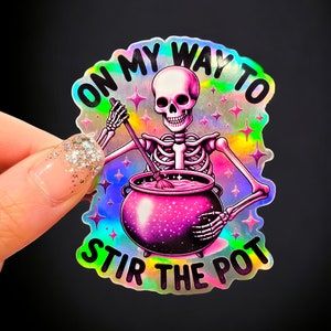 May include: A holographic sticker featuring a skeleton stirring a pink cauldron with the text "On my way to stir the pot".
