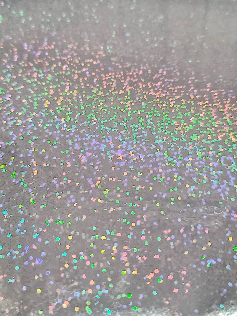May include: A close-up of a silver surface covered in iridescent glitter. The glitter is a mix of colors, including pink, green, blue, and purple.