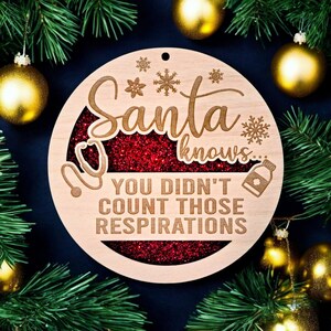May include: A wooden Christmas ornament with the words "Santa knows... You didn't count those respirations." The ornament has a red glitter center and snowflake and medical symbol designs. Gold ornaments and green pine branches surround the ornament.