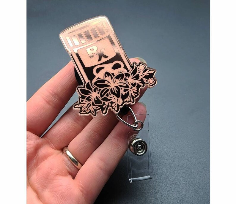 May include: Rose gold pill bottle charm with black floral details and a retractable badge holder.