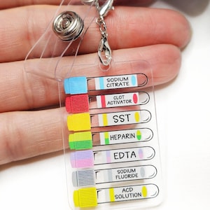 Op de afbeelding: Een doorzichtige plastic badge reel met een intrekbaar koord en een metalen clip. De badge reel heeft een ontwerp met een cartoon opossum en de woorden "DO IT!". Bevestigd is een doorzichtige plastic kaart met kleurgecodeerde bloedbuislabels.