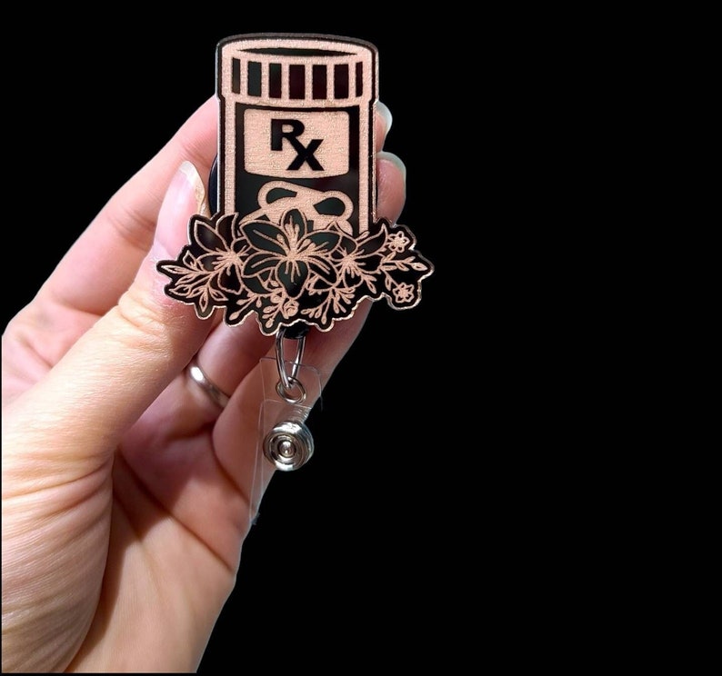May include: A black and rose gold retractable badge reel with a floral design and a pill bottle with the letters "RX" on it.