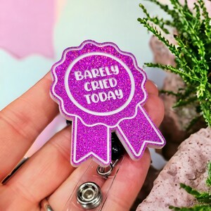 May include: A pink glitter badge holder with a white ribbon and the text "Barely Cried Today".